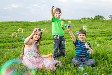 Three kids blowing up the soap bubbles on lawn