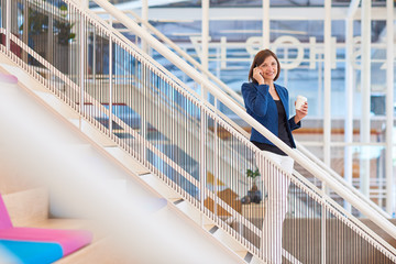 Smiling businesswoman on stairs in modern office with her phone