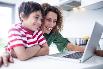 Mother and son using laptop in kitchen