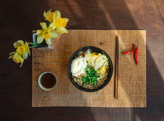 Chinese vegetarian noodles with egg, green onions and chili peppers on bamboo mat. Vintage dark wooden table. Top view