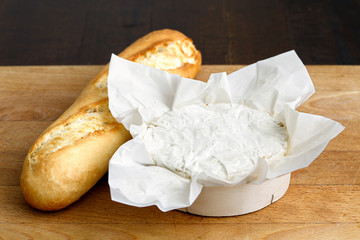 White mould cheese in wrapping with baguette on wood board.