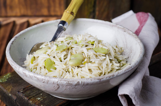Rice pilaf with fava beans on wooden background. Selective focus