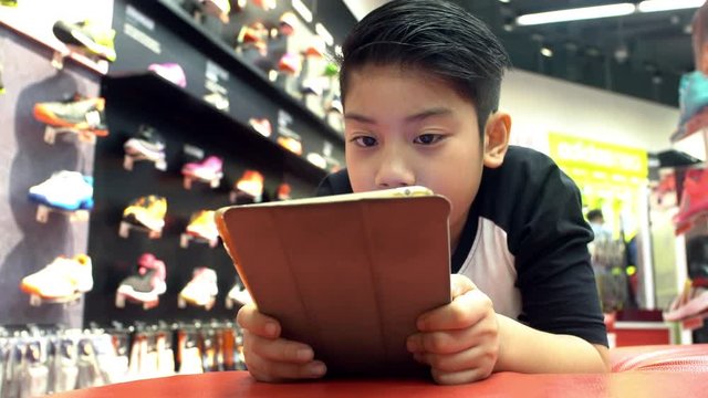 4K, Asian cute boy rest on floor and playing with tablet pc in shopping mall