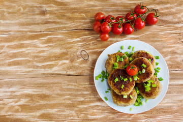 Roasted chicken cutlets with green onion on white plate and small cherry tomatoes on wooden background. Top view.