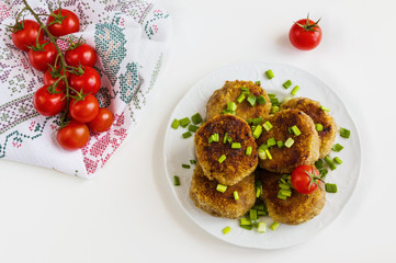 Roasted chicken cutlets with green onion on white plate and small cherry tomatoes on white table. Top view.