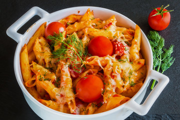 Pasta (penne) in white pan on black slate background. Vegetarian, cooked with tomatoes, garlic and cheese.