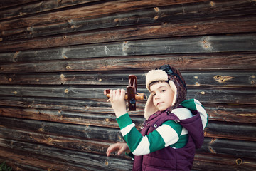 Boy playing in aviator hat with old plane at countryside
