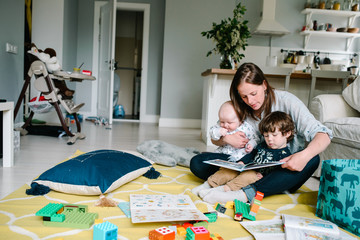Happy young mother reading a book to their children sitting in the floor of the house. The concept of family