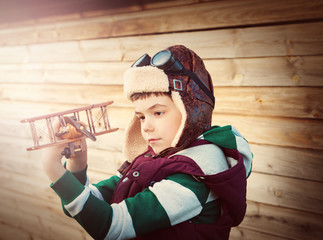 Boy playing in aviator hat with old plane at countryside