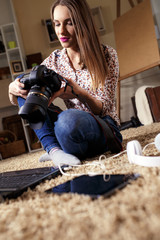 Young female photographer with laptop using modern dslr photo camera. Home interior.