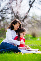 Happy Mom and daughter reading a book on nature