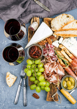 Cheese and meat appetizer selection or wine snack set. Variety of  cheese, salami, prosciutto, bread sticks, baguette, honey, grapes, olives, sun-dried tomatoes, pecan nuts over grey concrete textured