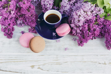 Cup of black coffee, lilac flowers and sweet pastel french macar