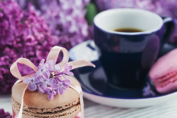 Cup of black coffee, lilac flowers and sweet pastel french macar