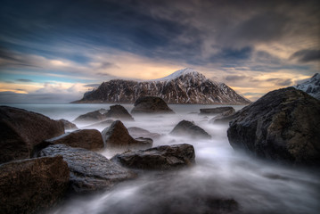 Rocks on coastline with Hustinden mountain and colorful clouds in background, Lofoten 