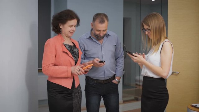 Colleagues in the hallway watching instagramm. They laugh, and discuss the photos and videos captured on the phone. 