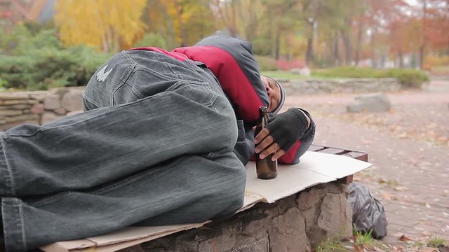 Drunk alcoholic sleeping on bench with empty bottle in hand, insolvent person