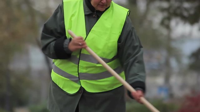 Unlucky senior woman sweeping street in autumn, working hard to get low wage