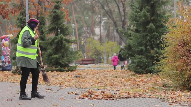Senior woman cleaning city park, stops to have rest, looking at beautiful autumn