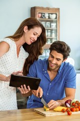 Woman using digital tablet and man chopping vegetables