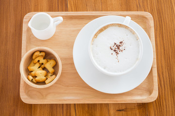 cappuccino in a white cup on a wooden plate with cookies on table