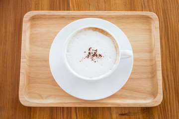 cappuccino in a white cup on a wooden plate on table