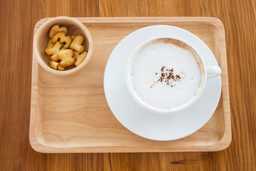 cappuccino in a white cup on a wooden plate with cookies on table