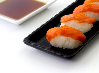 Salmon Sushi on the black plate with soy souse on a white table.