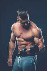 Fototapeta na wymiar Closeup of a muscular young man lifting dumbbells weights on dar
