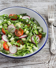 Fresh vegetable salad with cherry tomatoes, cucumbers, radishes and arugula. Healthy vegetarian food. On a light wooden rustic background