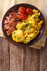 Breakfast is scrambled eggs with chives, fried bacon closeup. vertical top view
