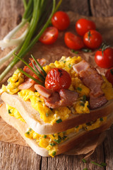 double sandwich with scrambled eggs, bacon and tomatoes close-up. vertical
