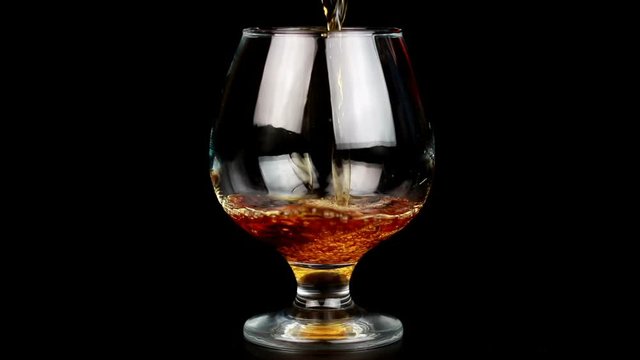 Close up of brandy being poured into snifter against black background