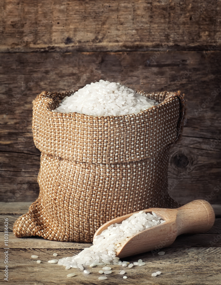 Wall mural rice in bag with scoop on wooden background