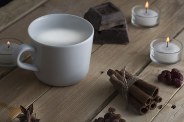 cup of steaming milk on old wooden boards, the board is chocolate, cinnamon, raisins