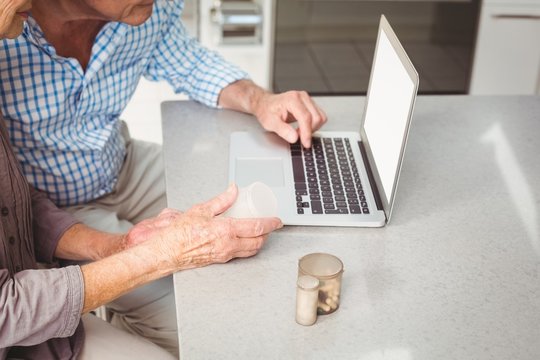 Cropped image of senior couple searching for pills on laptop