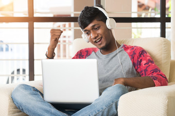 teenage indian male listening to music and using laptop