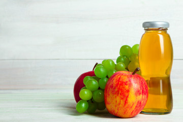 glass bottle of juice and an Apple with grapes on a white wooden background