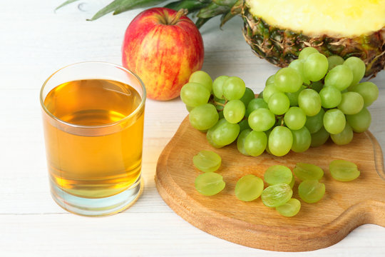 grape juice in a glass on a cutting Board with a bunch of grapes and apple with pineapple on white wooden table