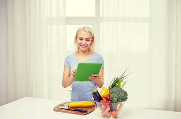 smiling young woman with tablet pc cooking at home