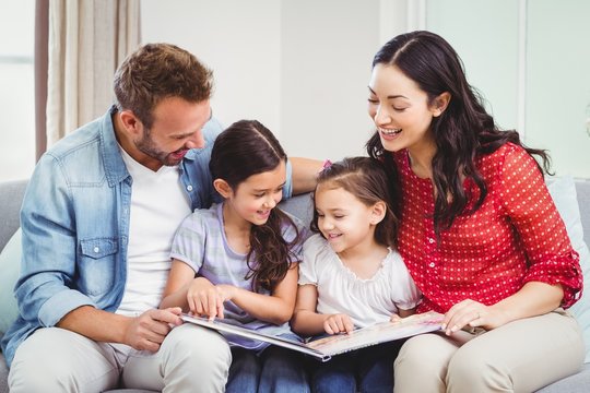 Parents looking in picture book while sitting with daughters