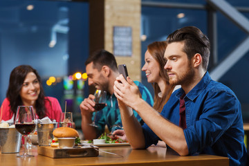man with smartphone and friends at restaurant