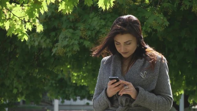 SheGirl in the park looking at your iPhone. She is looking for in his smarfone, lead hand on the screen hands the phone to watch