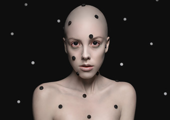 Bald headed girl with dots on face on dotted black background