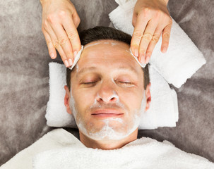 Male face with cream mask, hands of professional cosmetologist