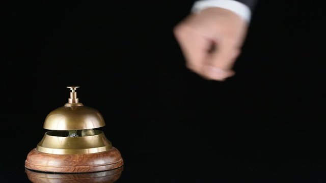 Hand ringing in service bell on wooden table on black background