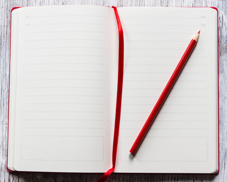 Red notebook with pencil on a white wooden background