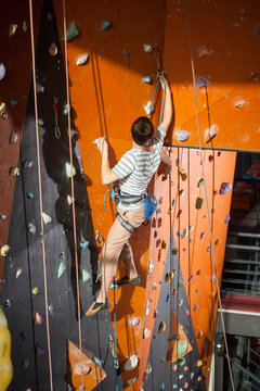 Climber young man climbing on practical wall indoor, securing carabiners and rope