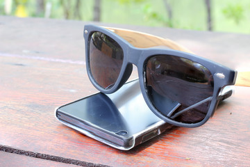 smartphone and Sunglasses on wood table.