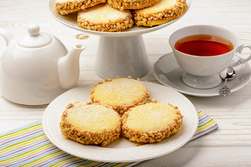 Butter cookies (alfajores) with caramel and peanut and cup of tea on wooden background.